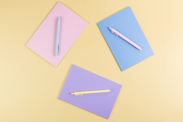 Top view of pink, purple and blue notebooks on yellow background. Pink, yellow and blue pens, school, office wallpaper. Flat lay, copy space.	