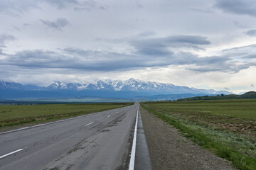 Road in the steppe with snow-capped mountains in the background