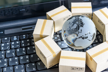 International freight or shipping service for online shopping or ecommerce concept : Paper boxes or carton put in circle around a clear crystal globe with world map on a computer notebook keyboard.