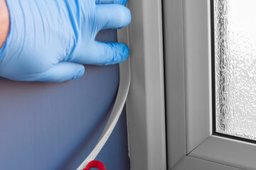 Person fixing self adhesive window seal to a upvc window frame. Energy efficiency saving concept