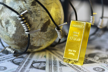 Gold bar lean against war barbed wire on USD bills beside blur globe . Gold is hard commodity goods, risk asset, tangible value that used to be gold reserve, save assets during war and economic crisis