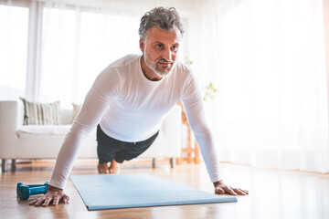 Obraz premium Handsome man exercising at home on gym mat, doing pushups. Routine home workout for a middle-aged man.
