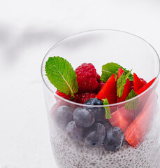 Chia pudding with fresh berries and mint in a glass standing on white table