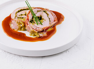 Gourmet stuffed pork roll with sauce on white plate
