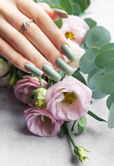 Elegant hand adorned with a ring showcasing stylish green nails beside a bouquet of soft pink and white flowers with greenery