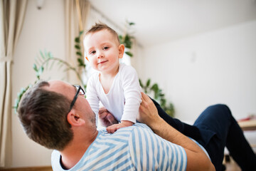 Portrait of father playing with little son, lying on floor and holding small boy above him.