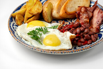 Delicious breakfast plate featuring eggs, beans, bacon, and potato wedges served on a decorative dish