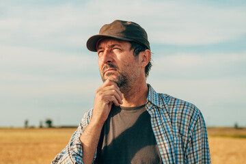 Portrait of male farmer standing in ripe wheat field and thinking