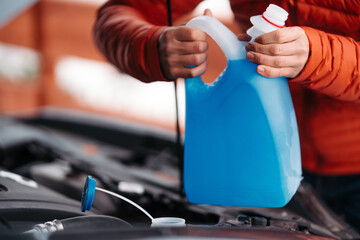 Pouring winter washer fluid into car reservoir during winter, protecting it from freezing.