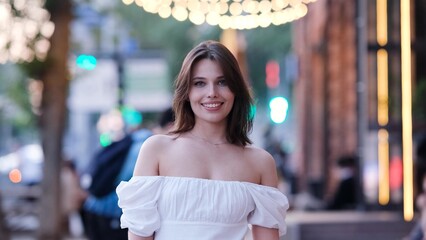 Portrait of a beautiful young woman in a cute white dress on a city street in the evening