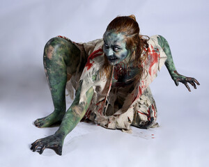 portrait of scary female model wearing spooky halloween costume, ripped clothes and fake blood like...