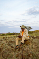 A young black woman sitting on a rock at sunset in a valley countryside