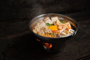 Tom Yum soup - Thai soup with crispy pork and minced pork and shrimp and squid noodles in hot pot on old wooden table