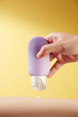 A model hand holds an unlabeled purple lotion bottle against a bright yellow background like a sun,...