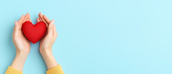 Heartfelt Gesture of Love and Care - Hands holding a red heart on light blue background with copy space. Concept of empathy and compassion.