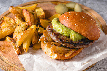 Burger with caramelized onion and avocado on a wooden cutting board