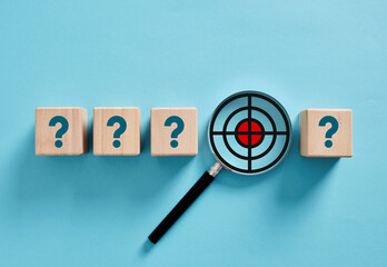 Magnifying glass focusing on target inside question marks on wooden cubes
