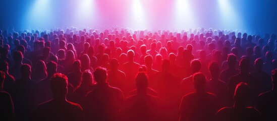 Crowd of people silhouetted against a stage lit with red and blue spotlights.
