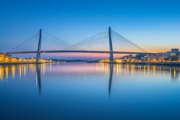 Obraz premium A stunning cable-stayed bridge spans a calm body of water, its elegant structure silhouetted against the dusk sky, perfectly mirrored in the water's reflection.