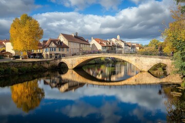 A scenic view of a charming town with a stone bridge arching gracefully over a reflective river, surrounded by trees and picturesque buildings basking in autumn light.