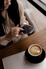 woman in a cafe with a phone and laptop drinking a cup of coffee, top view _ image