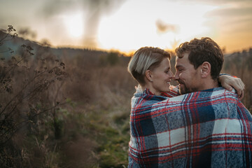 Fototapeta premium Couple in love on a walk in autumn forest. Husband and wife standing in the middle of meadow covered in warm blanket.