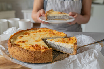 Homemade poppy seed cake with sour cream topping served by a woman with apron in the kitchen