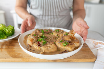 Homemade fresh cooked turkey breast in a delicious onion cream sauce served by a woman in the kitchen