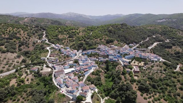 Aerial view of a mountain village with colorful rooftops, winding roads, and lush green hills, Juscar, Malaga, Andalucia, Spain
