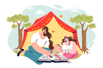 Family camping on summer vacation with mother reading book to daughter, sitting near tent in parks