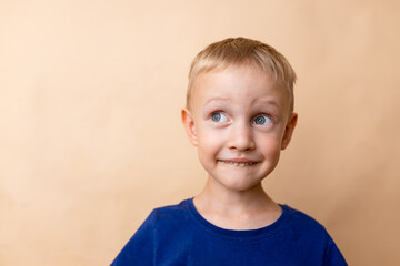 A cheerful young boy with short blonde hair and blue eyes makes a playful expression against a...