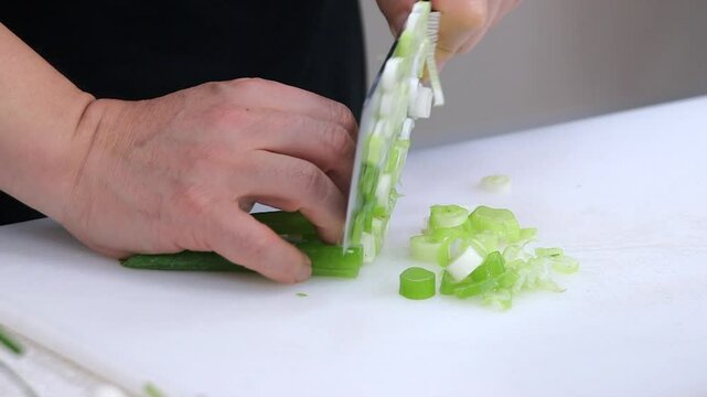 흰 도마 위에서 칼로 신선한 파를 자르는 모습