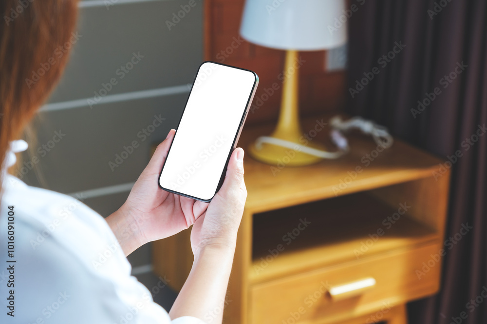 Wall mural Mockup image of a woman holding mobile phone with blank desktop white screen at home