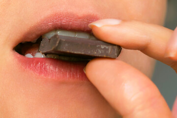 close-up of a person biting into a piece of dark chocolate, highlighting the rich flavor and...