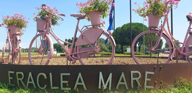 Pink bicycles with pink pelargonium flowers stand at the entrance to the town of Eraclea mare. Panorama.