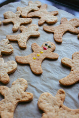 Gingerbread man cookies on baking tray. Decorated cookie with smile and eyes. Christmas cookies background. Homemade biscuits. Cinnamon cookies on baking paper. Funny ginger men biscuits.