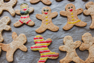 Gingerbread man cookies on baking tray. Decorated cookie with smile and eyes. Christmas cookies background. Homemade biscuits. Cinnamon cookies on baking paper. Funny ginger men biscuits.