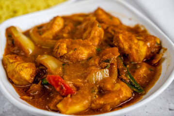 Delicious plate of chicken curry was served in a white bowl, showcasing tender chicken pieces in a rich, spicy sauce with visible vegetables and herbs.