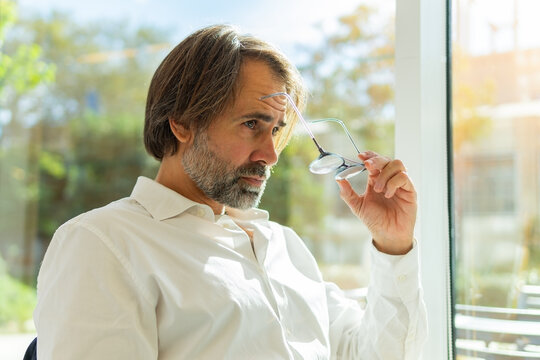 Thoughtful businessman holding glasses in office setting