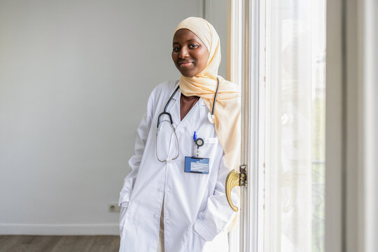 Black female doctor in white coat and hijab by window