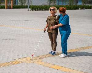 A nurse accompanies an elderly blind woman on a walk.