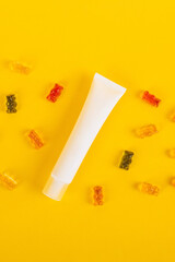 Cosmetic product in tube, bottle, lotion or serum and colorful candies, jelly on yellow background. 