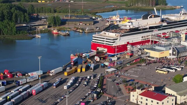 Aerial view of a large cruise ship docking at the port of Turku, Finland. Passengers, trucks and cars are disembarking the ship as tourists wait to board