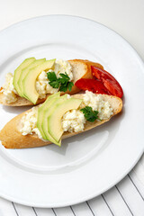 Fresh avocado and cheese spread on toasted bread garnished with cilantro and tomato