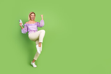 Photo of crazy cheerful girl wear stylish clothes hand hold modern device empty space isolated on green color background