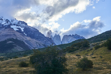 Torres del Paine in Patagonia, Chile, with its jagged granite peaks rising above the forested landscape, shrouded in dramatic clouds and mist.