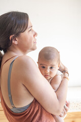 A woman holds a baby in her arms in a relaxed and thoughtful pose.