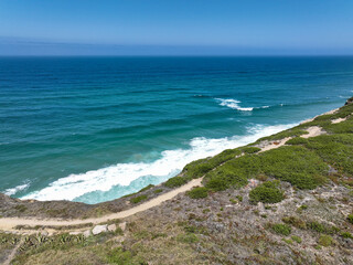 A winding path leads to the edge of a cliff offering stunning views of the turquoise ocean and crashing waves