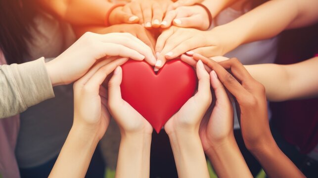 A diverse group of people joyfully holding a large red heart symbol, representing unity, teamwork, and community spirit, with hands intertwined.