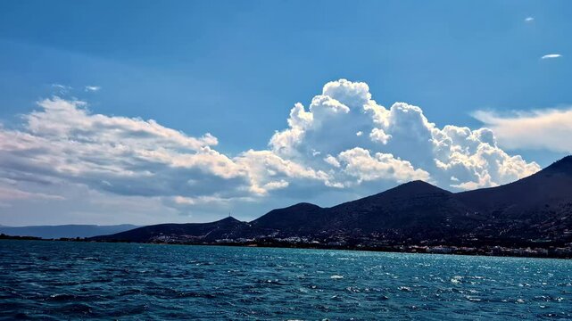 Picturesque view of cumulus, fluffy clouds over a mountain with oceanfront in Greece on a summer afternoon. Seascape.